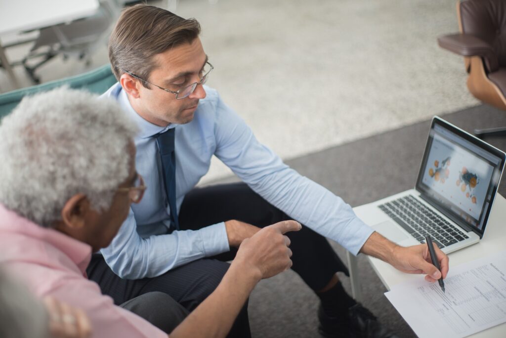 One person pointing at a printed form while another looks on, a laptop open beside them.
