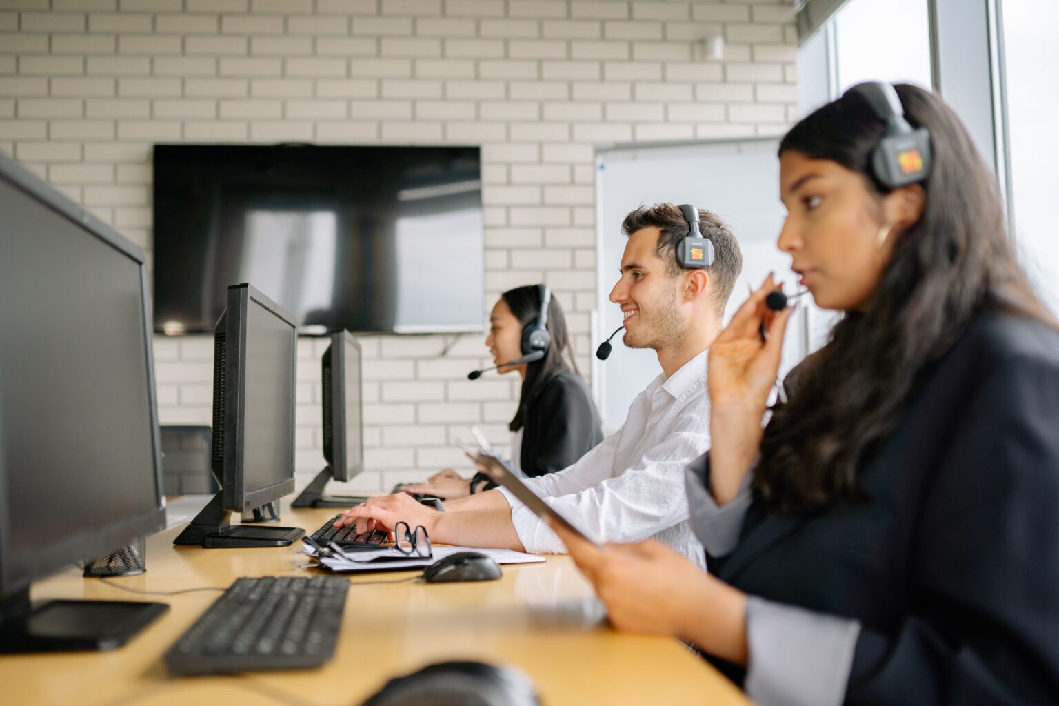 Three people wearing telephone headsets at a row of desks, taking calls.