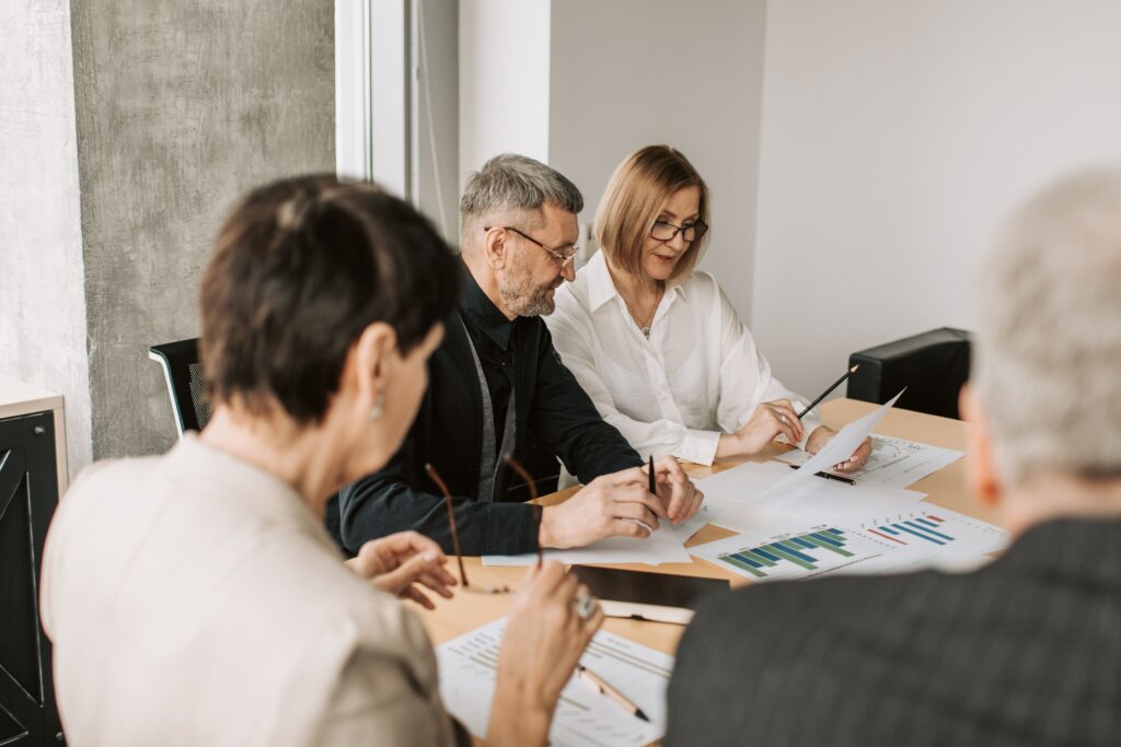 Several people leaning over printed charts on a meeting table, discussing them.